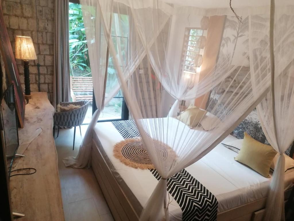 Chambre avec lit à baldaquin et moustiquaire, mur en pierre, lampe en fibre naturelle et fenêtre sur le jardin