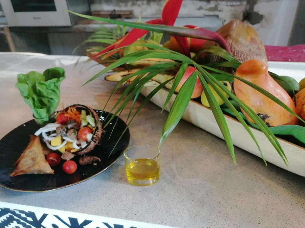 Entrée dressée sur assiette noire, samoussa et salade en noix de coco, devant un plateau de fruits décoré de palmes