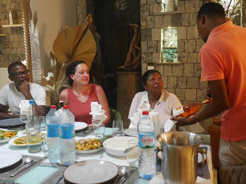 Repas partagé à la table d'hôtes : convives attablés et service du vin dans la salle à manger aux murs de pierre