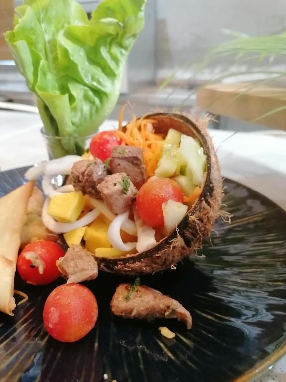 Salade servie dans une demi-noix de coco : dés de viande, mangue, tomates cerises et concombre