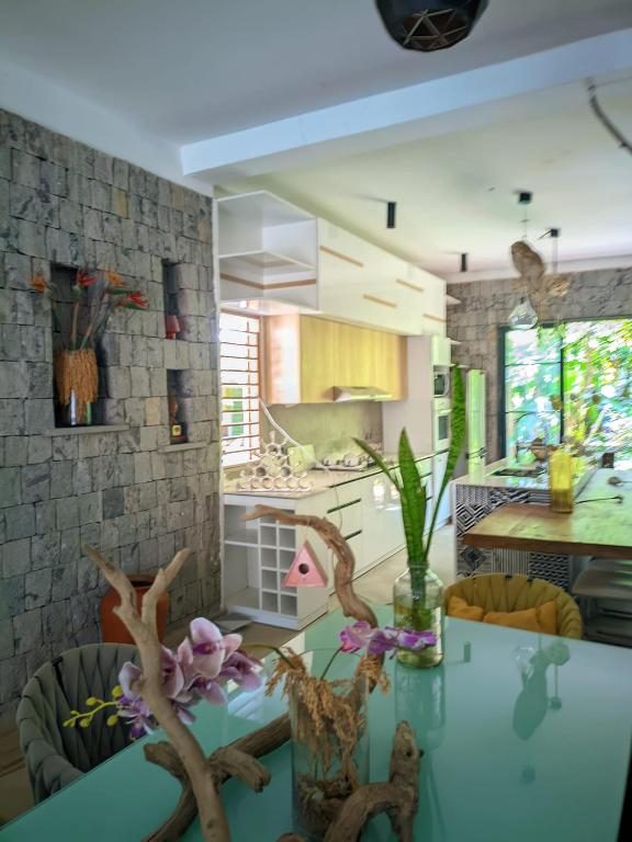Salle à manger et cuisine ouverte : table en verre décorée d'orchidées et de bois flotté, murs en pierre